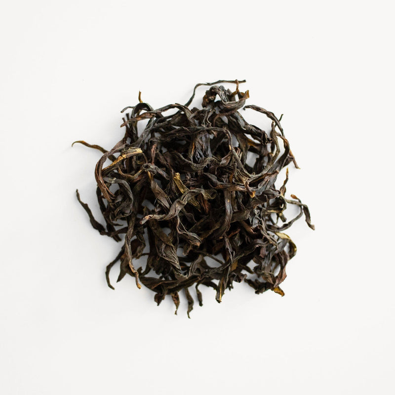 A pile of Rishi Tea & Botanicals Phoenix Dancong Mi Lan Xiang black tea on a white surface.