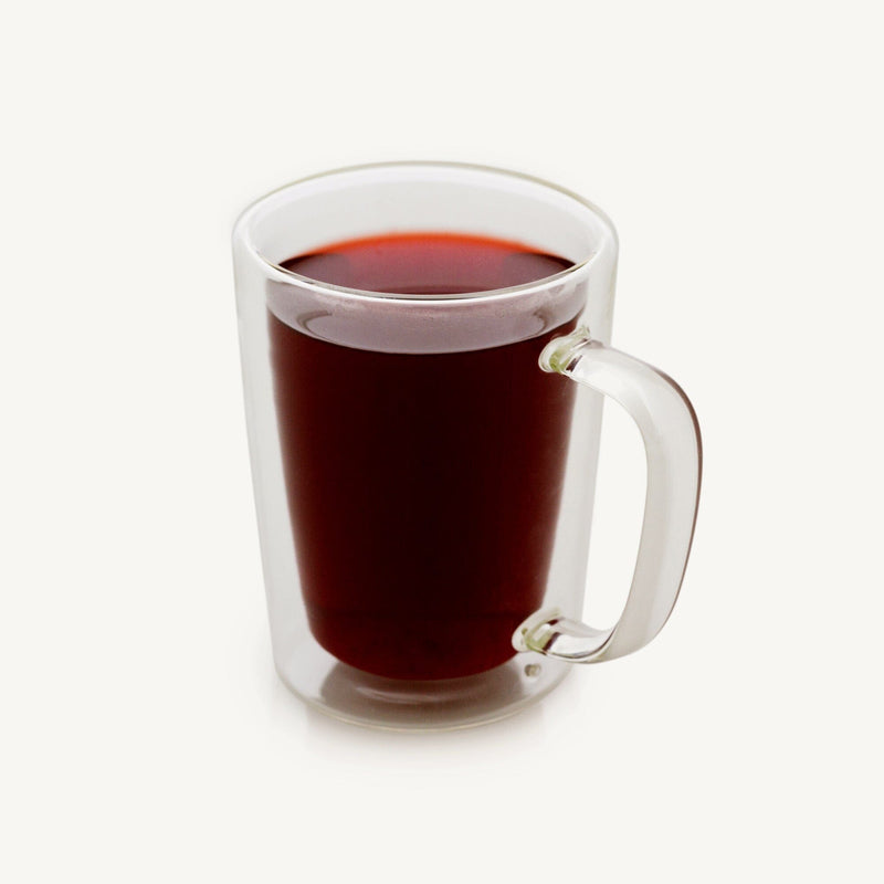 A hot tea-filled Rishi Tea & Botanicals Double Wall Glass Tea Mug placed on a white surface.