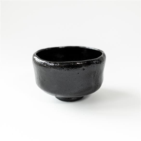 A small Kuro Raku Yaki Matcha Bowl sitting on a white surface.