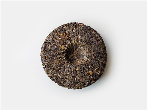 A piece of Cangyuan Sheng Tea Cake Vintage 2021 from Rishi Tea & Botanicals on a white surface.