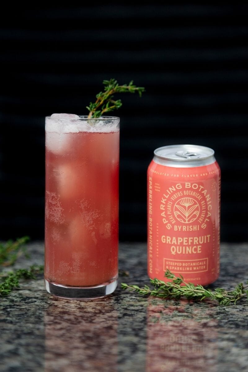 Grapefruit Quince & Thyme in a tall glass with thyme as a garnish next to the Grapefruit Quince Sparkling Botanical can.