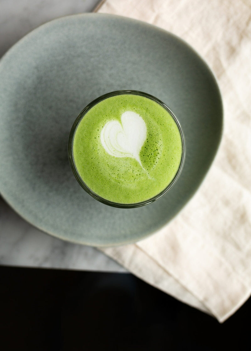 Top view of a bright green matcha cappuccino with a heart shape in the foam