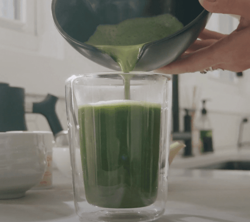 Matcha tea shot being poured over Sensa infused tea in glass cup.