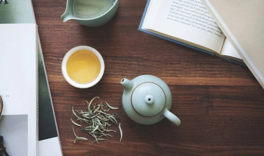 Teapot on table with tea leaves, cup and books