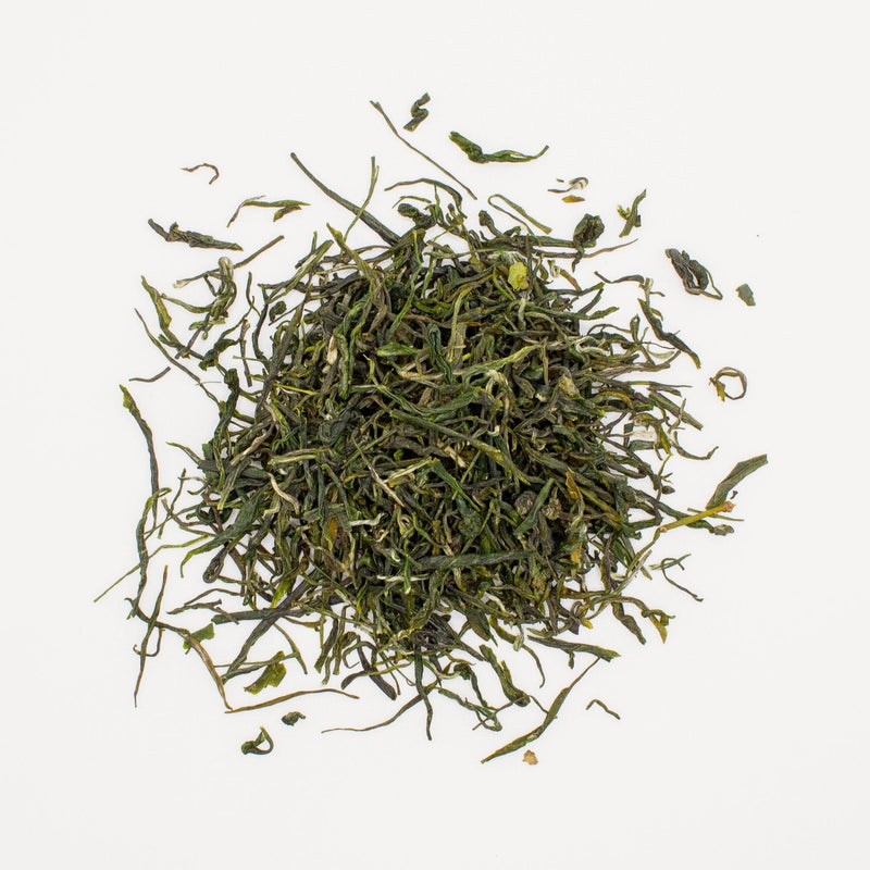 A pile of loose Green Needles Qun Ti Zhong tea leaves scattered on a white background. (Rishi Tea & Botanicals)