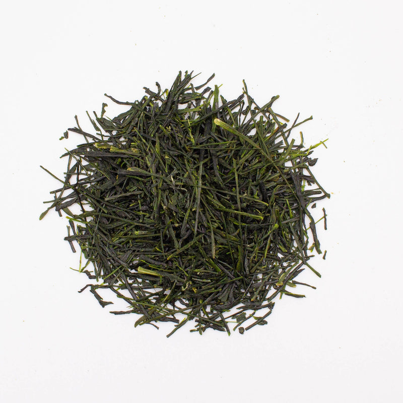 A pile of loose, dark green Nishi San’s Hand-Picked Saemidori Shincha harvested by hand from Rishi Tea & Botanicals rests on a white background.