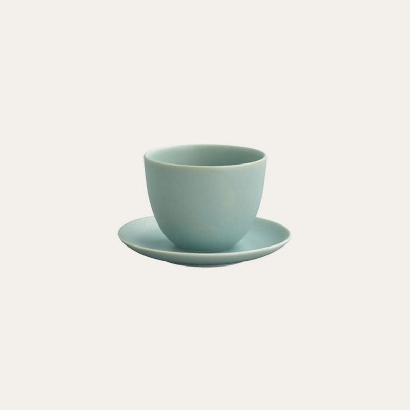 The Kinto Pebble Porcelain Teacup & Saucer by Kinto USA, Inc is featured against a plain background, showcasing its light blue color and durable porcelain construction, both microwave and dishwasher safe.