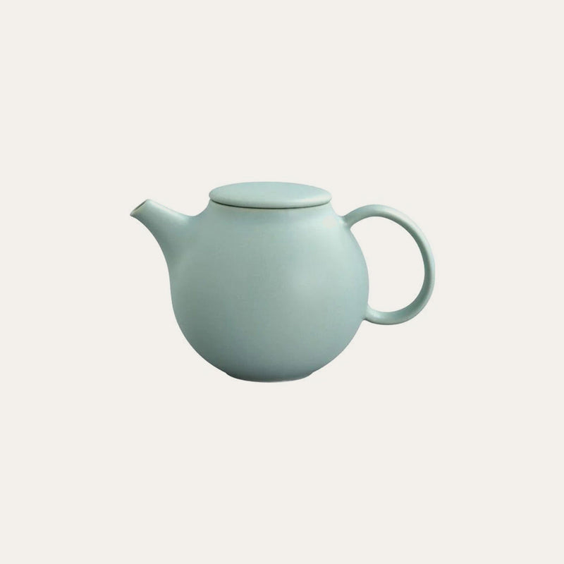 A small, round, light green porcelain Kinto Pebble teapot by Kinto USA, Inc., featuring a lid, handle, and short drip-free spout with a built-in stainless steel strainer, set against a plain light background.