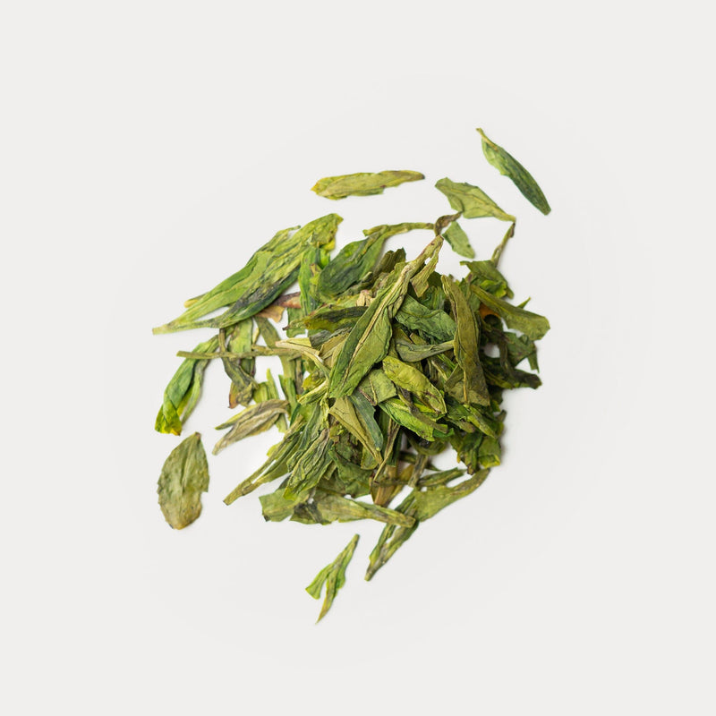 A pile of Dragon Well green tea leaves on a white background from Rishi Tea & Botanicals.