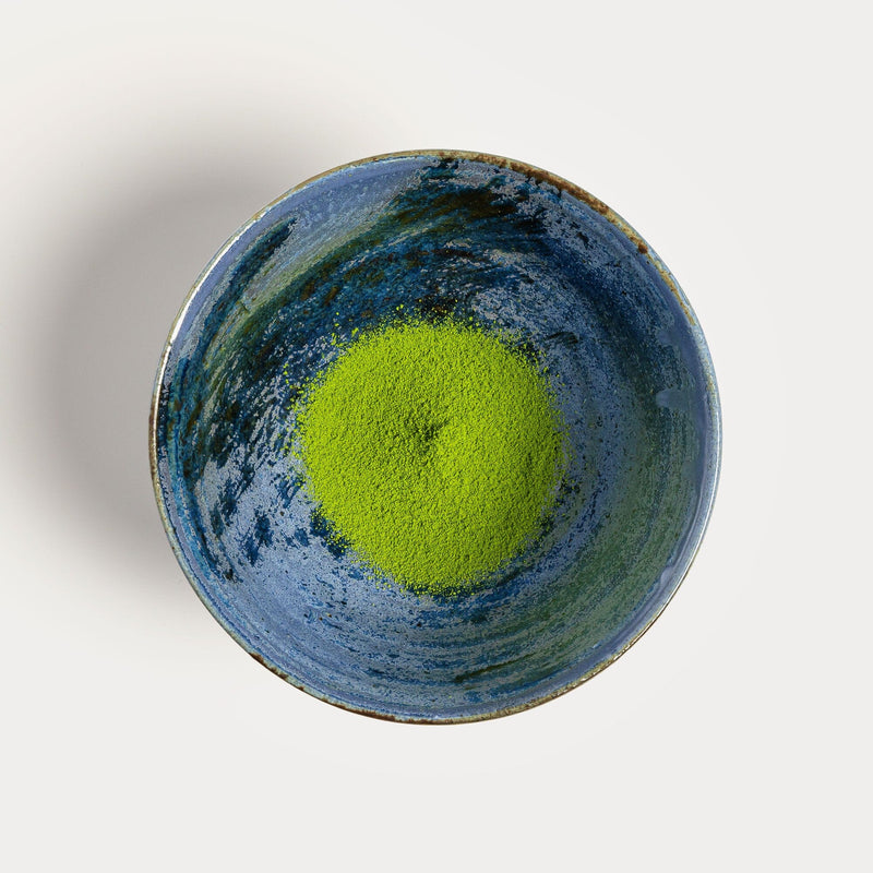 A bowl of green Matcha Okumidori by Rishi Tea & Botanicals on a white surface.