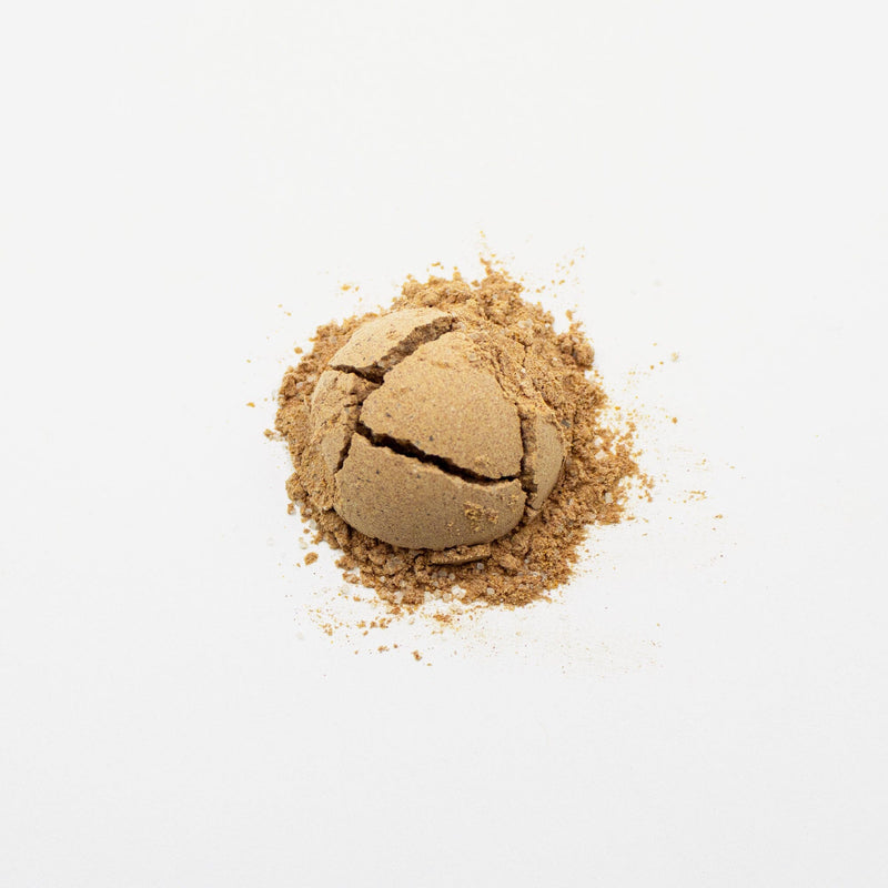 A cracked ball of compacted sand isolated on a white background with natural beet coloring is the Sweet Thai Tea Powder from Rishi Tea & Botanicals.