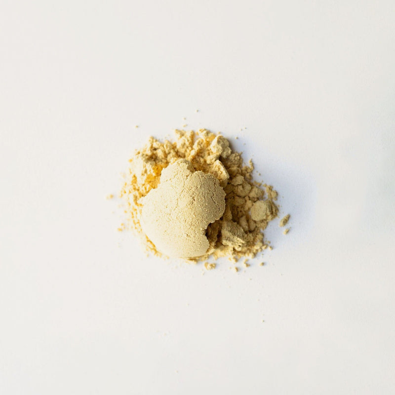 A small pile of beige powder, likely Bamboo Ginger Powder from Rishi Tea & Botanicals, known for its health benefits, rests on a white background.