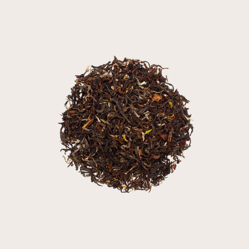 A mound of Darjeeling Second Flush Pussimbing DJ65 loose leaf tea from Rishi Tea & Botanicals, showcasing the rich hues of black tea, set against a simple beige background.