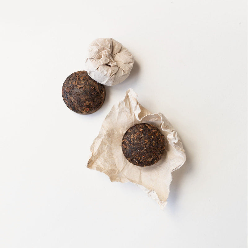 Two wrapped Pu'er Tuo Cha Schisandra Clove tea balls and two unwrapped ones from Rishi Tea & Botanicals rest on a white surface.