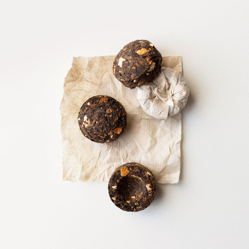 Four Pu’er Tuo Cha Tangerine Peel tea cakes from Rishi Tea & Botanicals sit atop a crumpled piece of paper against a white background, offering an intricate taste profile that excites the palate.