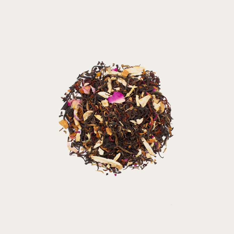 A heap of Rose Ginger Cinnamon Black Tea by Rishi Tea & Botanicals, with visible dried rose petals and other mixed dried ingredients, exuding the scent of aromatic red roses on a plain background.