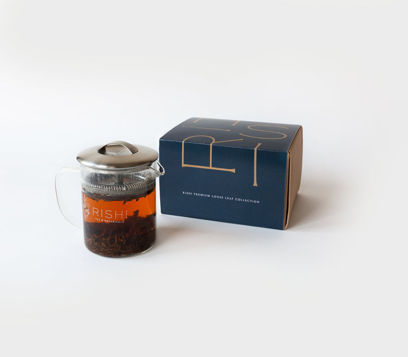 A glass teapot filled with tea sits beside a blue and orange box labeled 