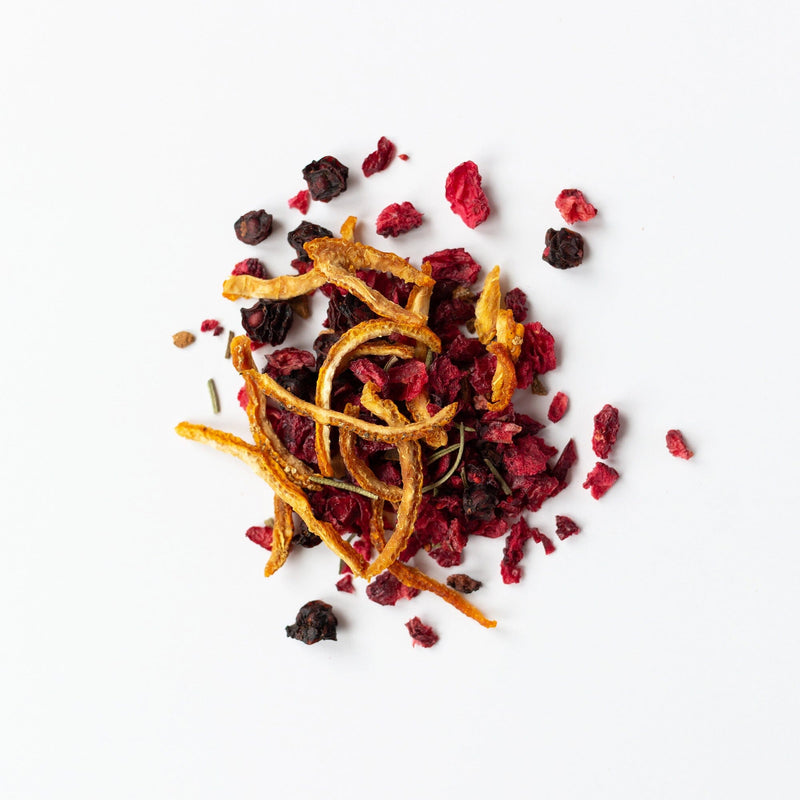 A vibrant mix of dried tea ingredients, featuring the Cranberry Yuzu blend by Rishi Tea & Botanicals, showcasing orange peels, cranberries, red berries, and a touch of cinnamon spice against a white background.