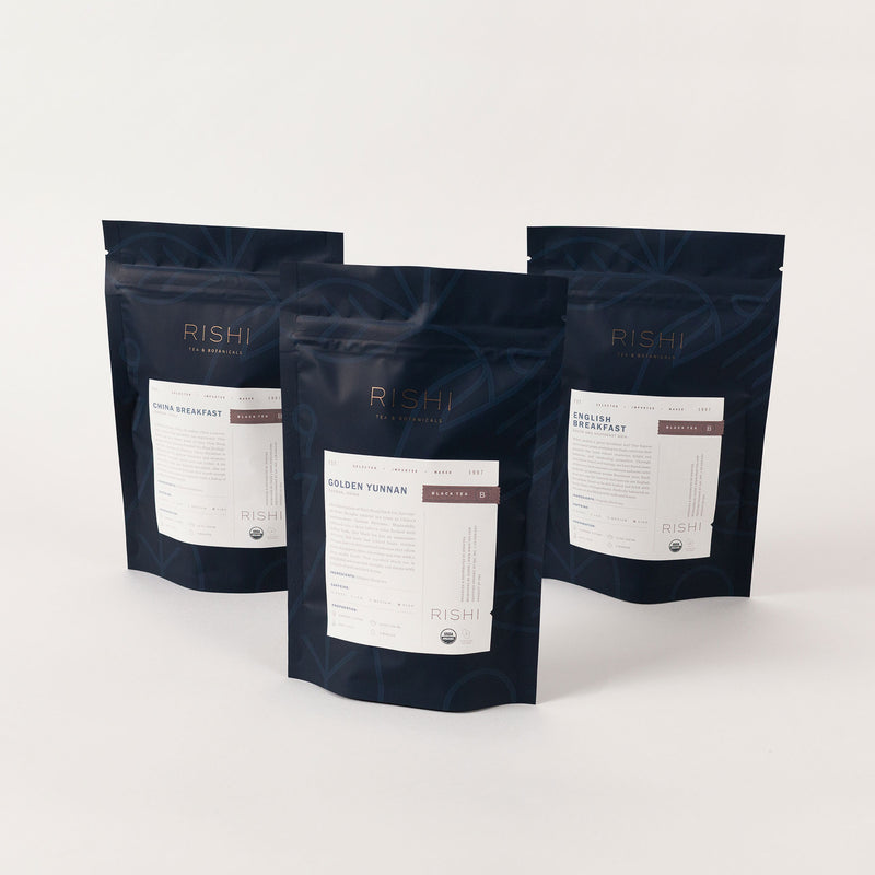 Three dark blue pouches from Rishi Tea & Botanicals are arranged upright, highlighting their enticing Breakfast Flight of Tea Bundle. Ideal for elevating your morning routine, this bundle features a selection of organic black teas set against a plain background.