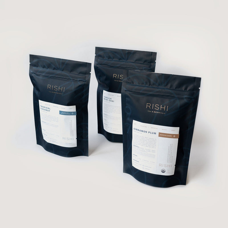 Three black packages from the Rishi Tea & Botanicals collection are showcased within the Tea for Dessert Flight of Tea Bundle, featuring Tropical Green, Jasmine Green, and Cinnamon Plum flavors, each offering a unique taste adventure.