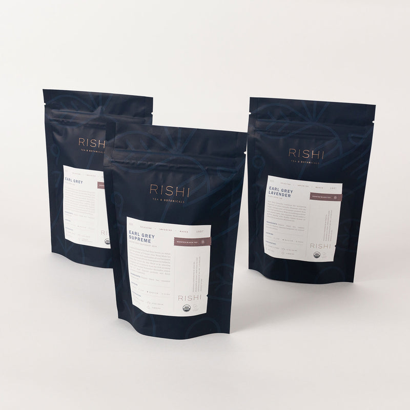 A stylish tea bundle, the Earl Grey Flight of Tea Bundle, showcases three dark-colored standing pouches, each adorned with the elegant Rishi Tea & Botanicals label. Experience the exquisite Earl Grey Lavender blend, where fragrant bergamot beautifully harmonizes with soothing lavender.