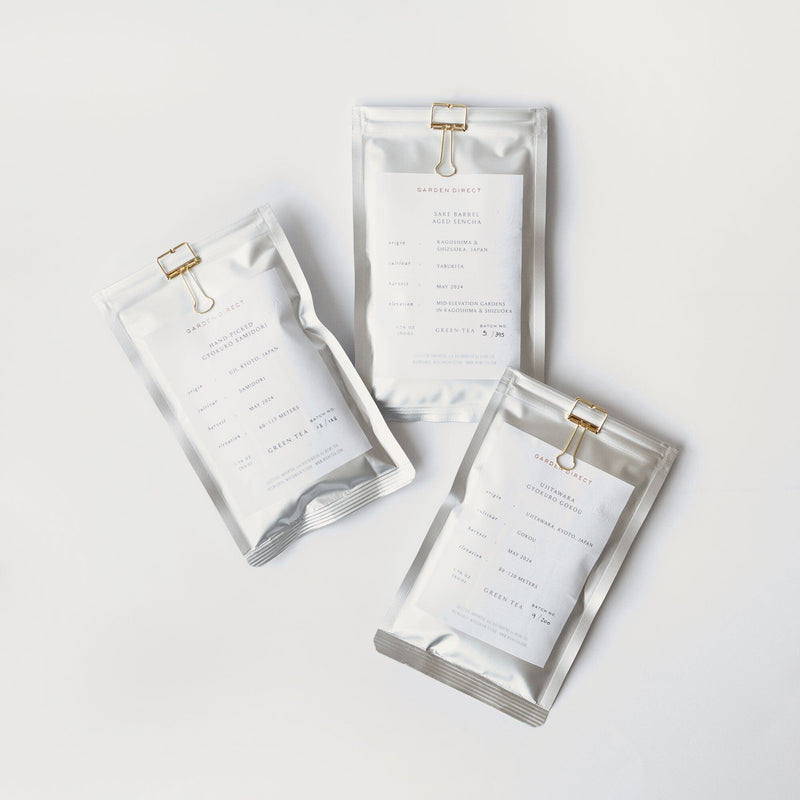 Three silver pouches from the Kuradashi Flight of Tea Bundle by Rishi Tea & Botanicals, featuring white labels and gold clips, are artfully displayed on a white background, capturing the refined elegance of Japanese green tea.