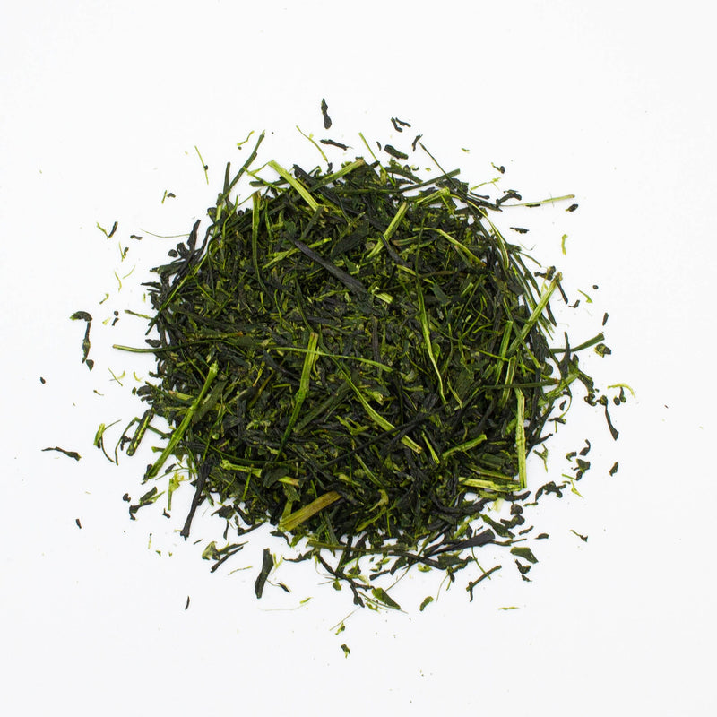 A pile of loose Shincha Asatsuyu green tea leaves from Rishi Tea & Botanicals, known for their umami taste, lies on a white background.
