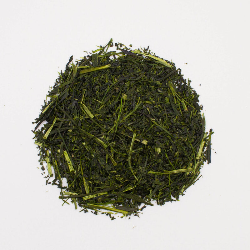 Loose-leaf green tea from Saemidori garden in a pile on a white background. The finely chopped leaves are dark green, reminiscent of the premium Shincha Saemidori from Rishi Tea & Botanicals.