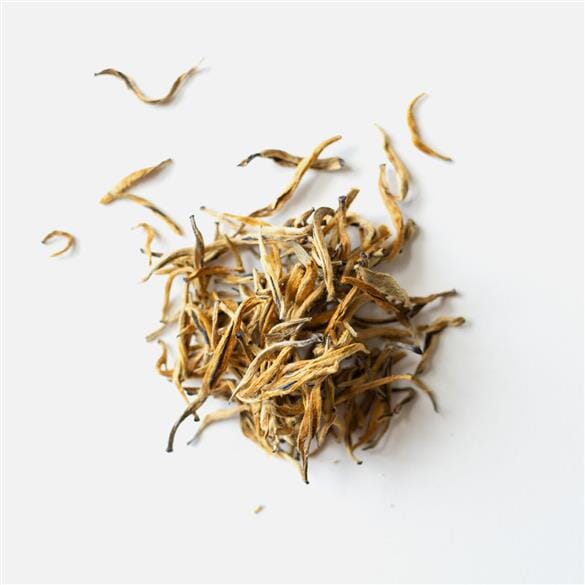 A pile of Yunnan Dian Hong Golden Buds tea leaves on a white surface, from the brand Rishi Tea & Botanicals.